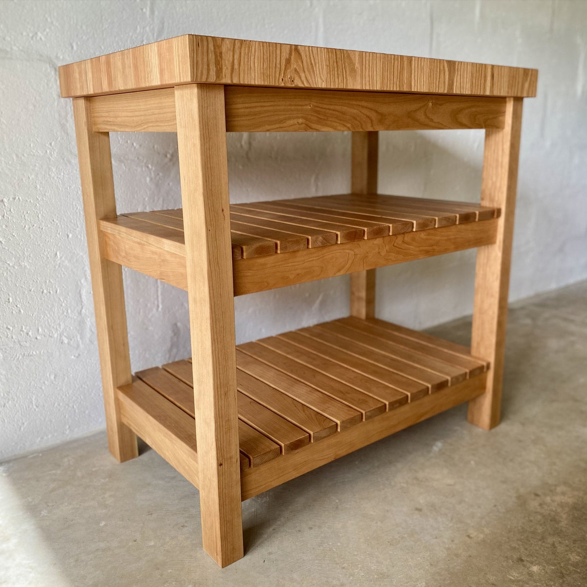 American cherry end grain butcher's island with two slatted shelves, angled view against white wall – East Wood Design