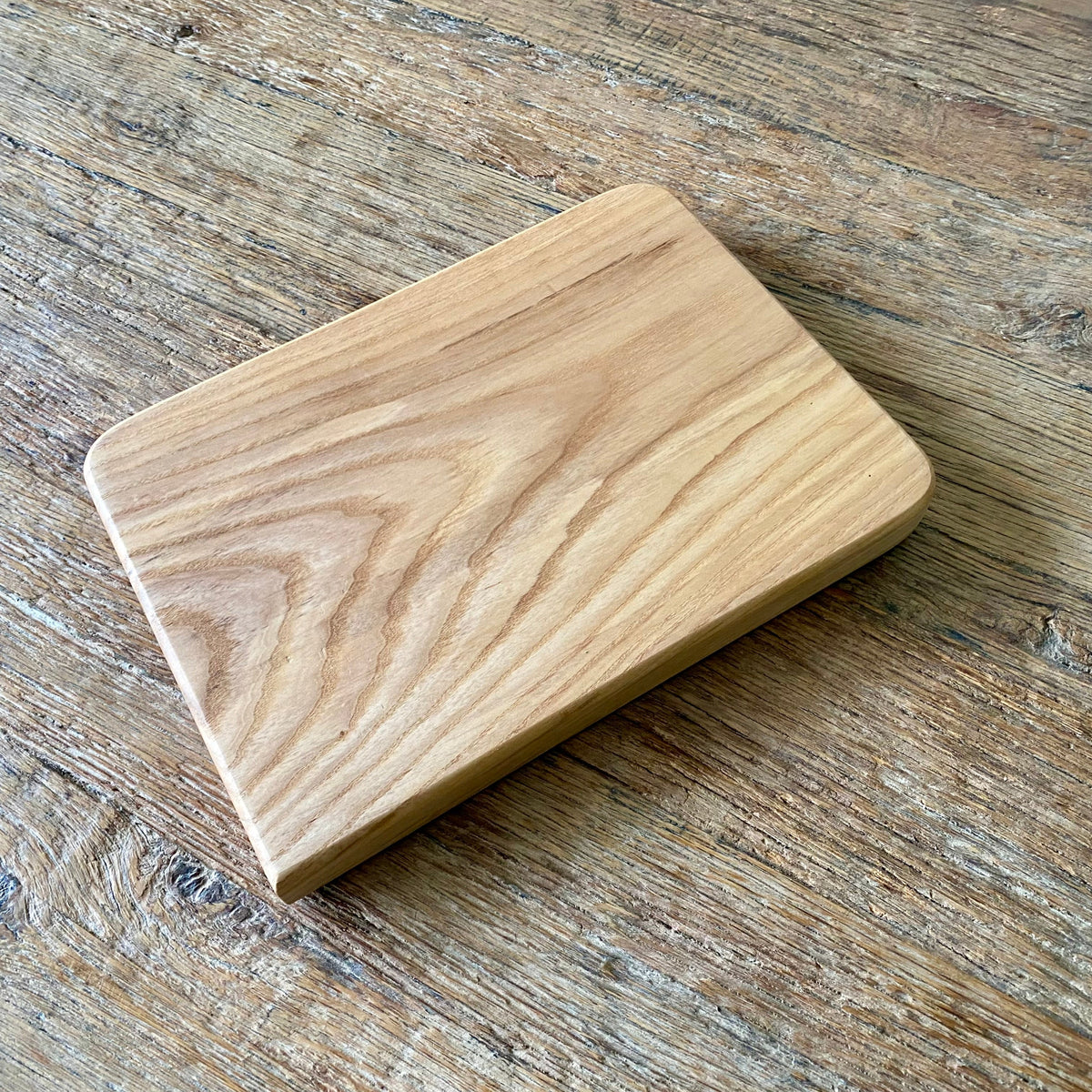 A rectangular Ash wood cutting board with rounded corners. Angled view showing natural ash grain