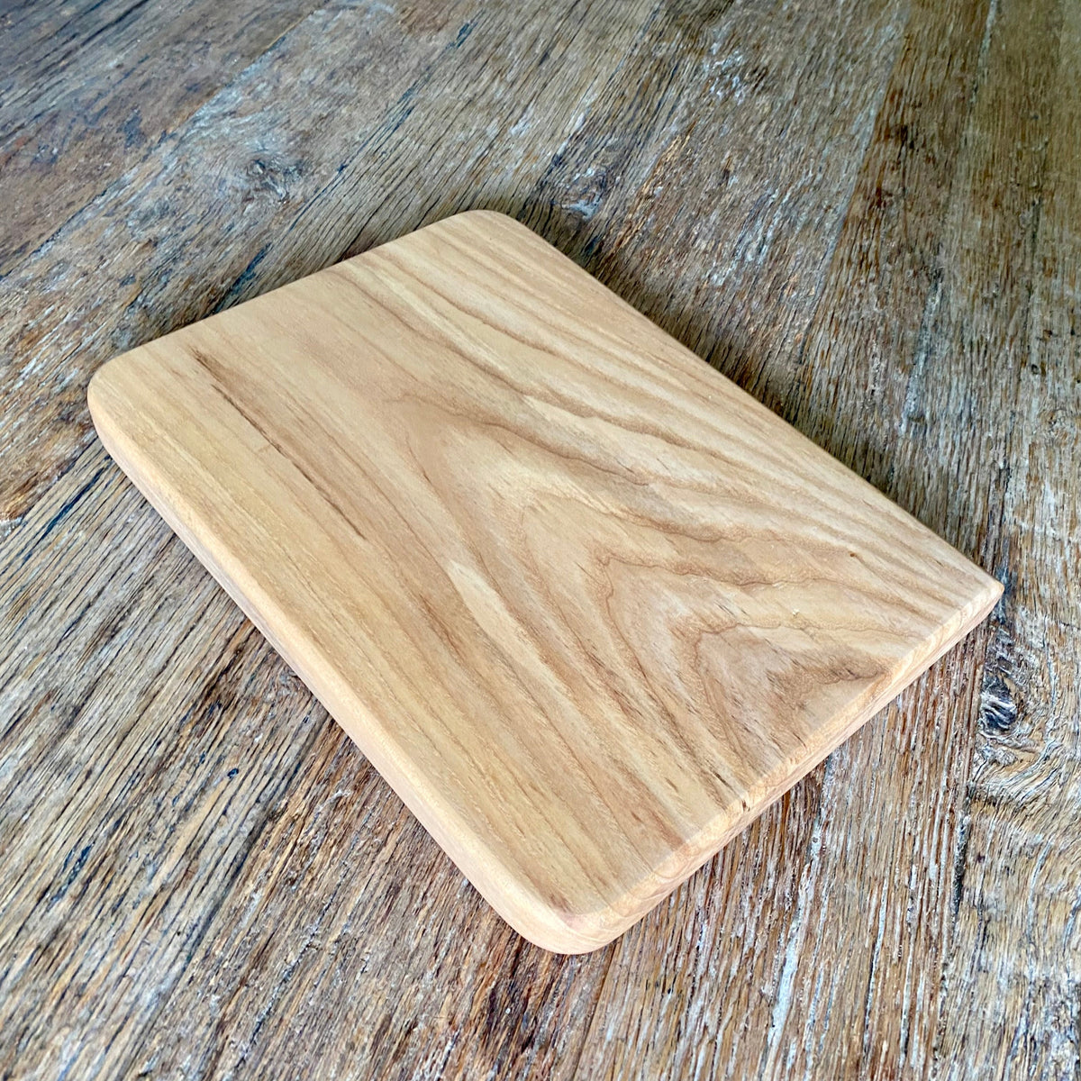 A rectangular Ash wood cutting board with rounded corners, laying on a rustic table