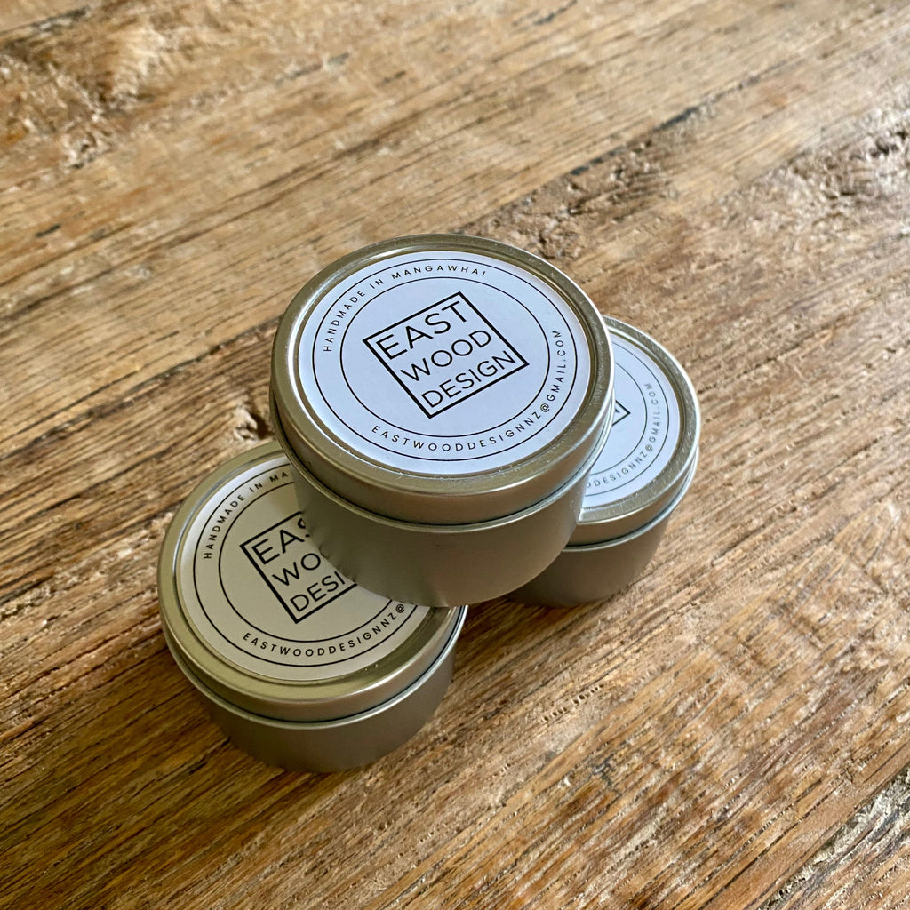 Three small round metal tins of beeswax mineral oil conditioner with white lids printed with the brand name 'East Wood Design' arranged on a rustic wooden tabletop.