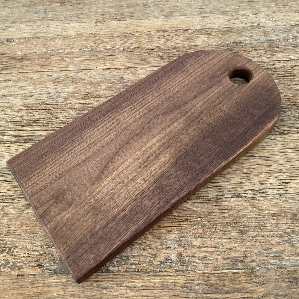 Black walnut arc platter tag shape angled flat lay on rustic timber surface showing rich dark grain – East Wood Design