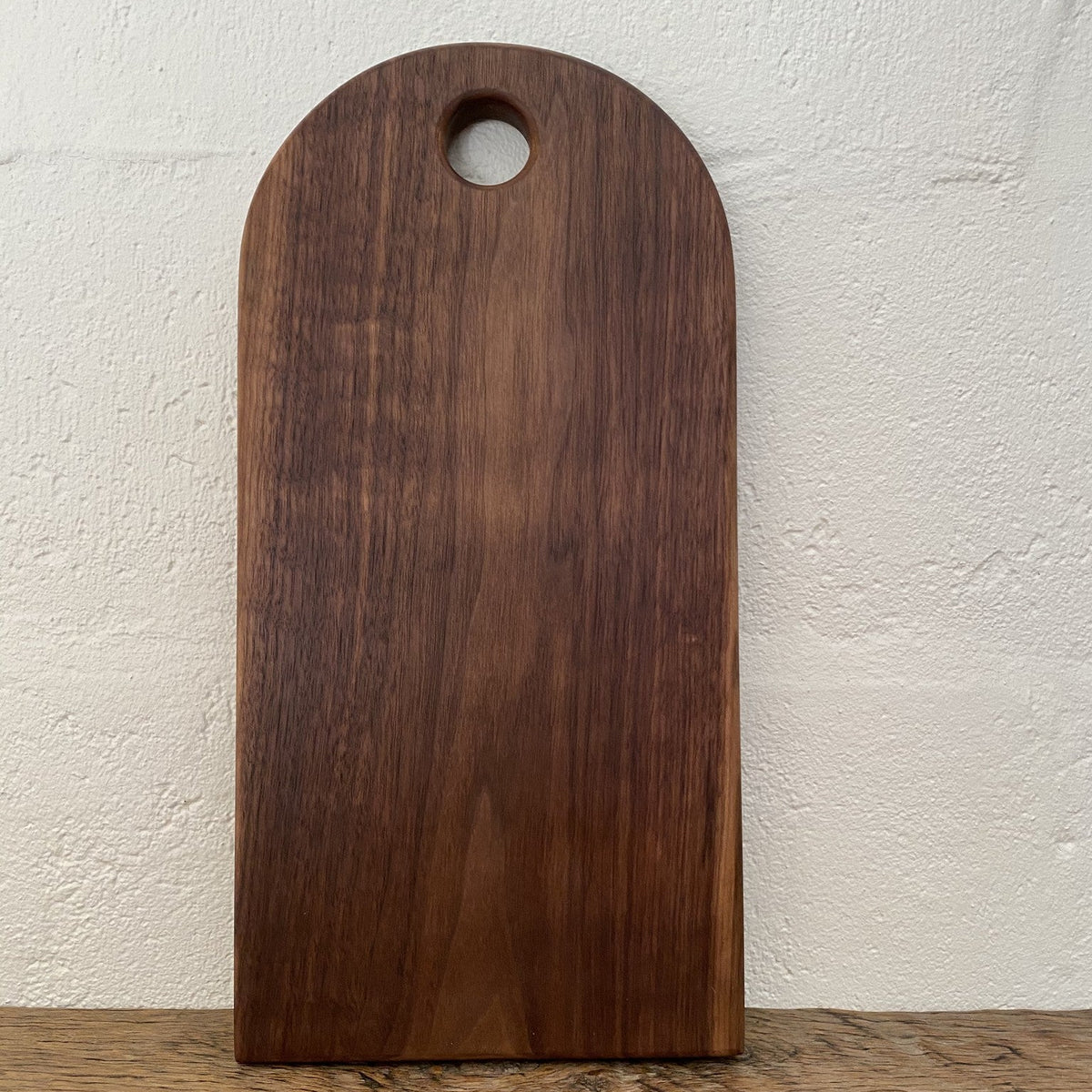 Black walnut arc platter arch shape leaning against white wall showing full profile and finger hole – East Wood Design