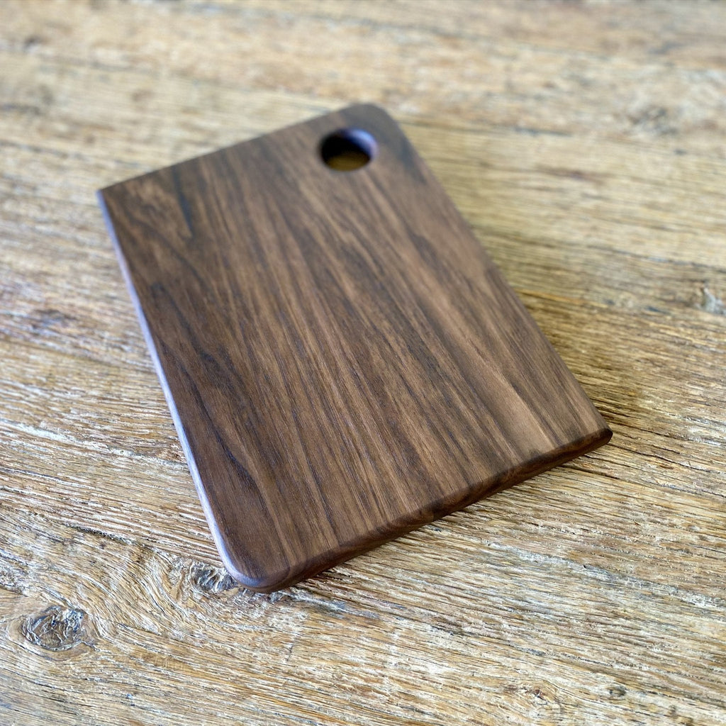 Small black walnut chopping board angled view showing rich dark grain and finger hole – East Wood Design