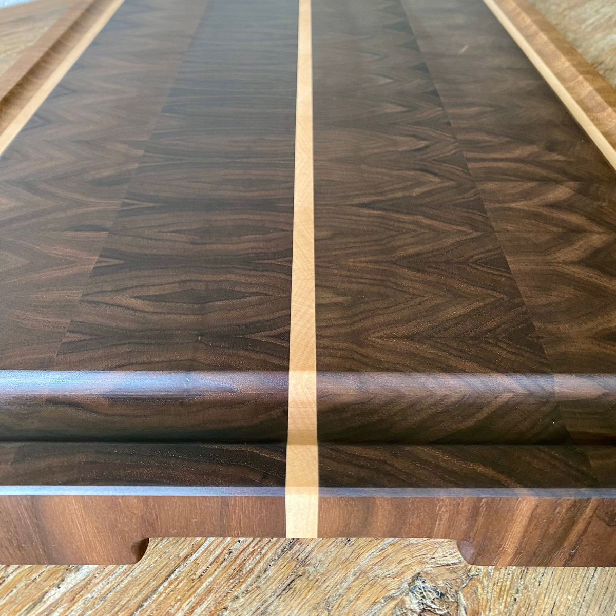 A close-up of a wooden Black Walnut cutting board with a dark brown and black wood grain pattern, featuring a light beige centre stripe and a matching light wood edge.