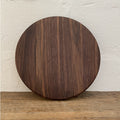 The Round Black Walnut serving board – angled lifestyle view on rustic timber surface