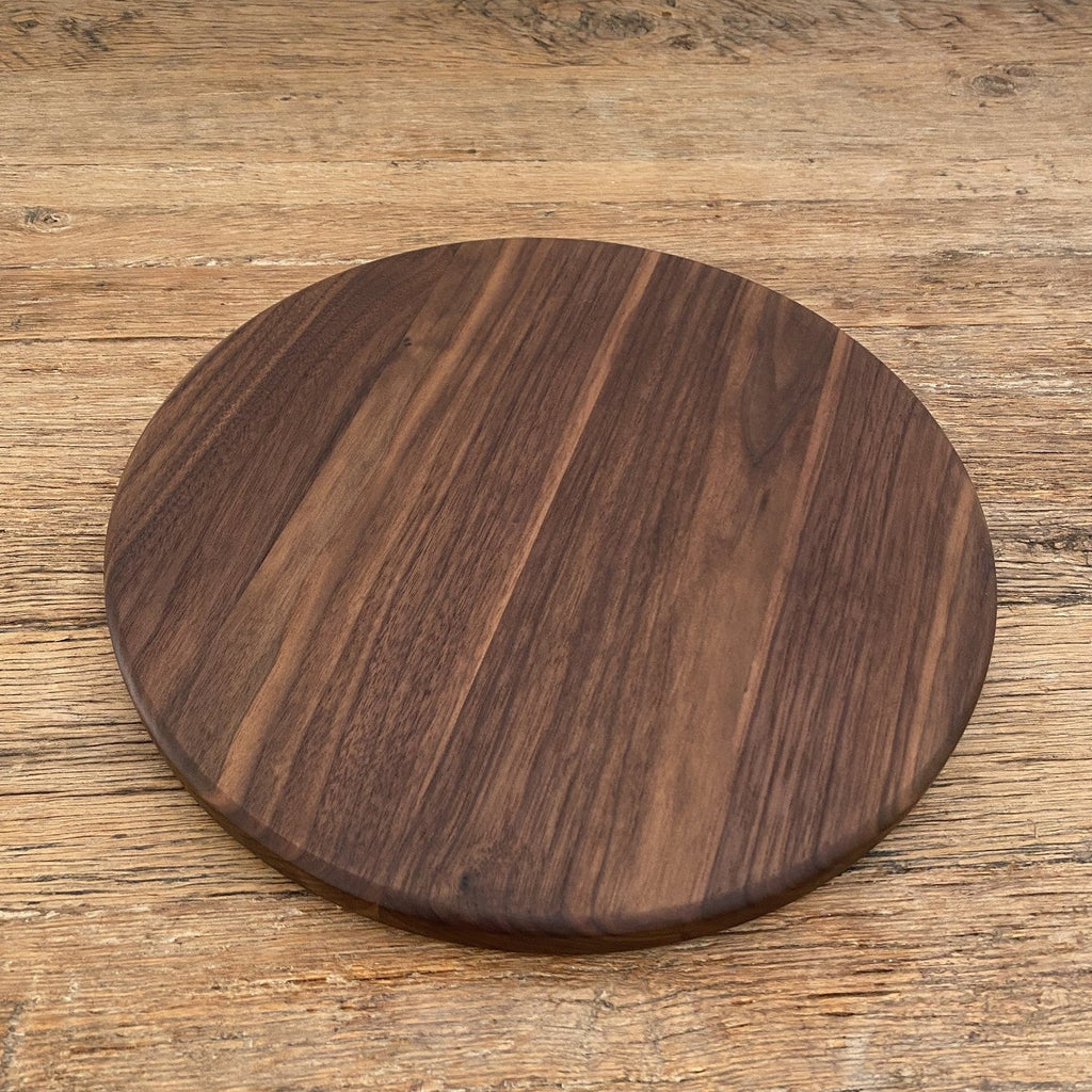 The Round Black Walnut serving board – upright against white wall showing grain detail