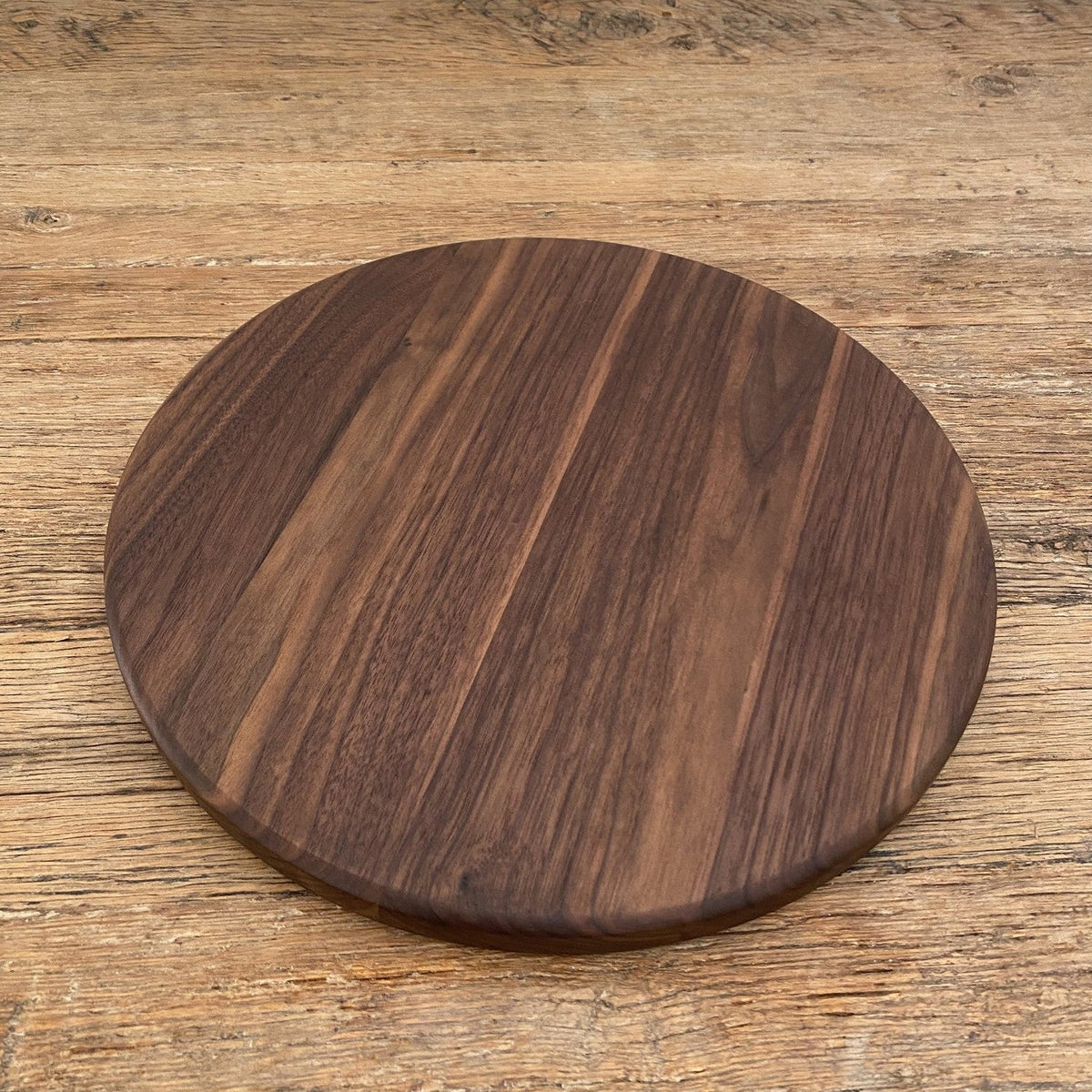 The Round Black Walnut serving board – upright against white wall showing grain detail