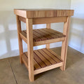 A end grain butcher island, made from pacific rimu with a middle slatted shelf, and a bottom slatted shelf, photographed in a room corner.