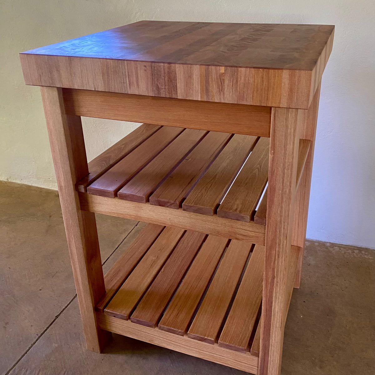 A end grain butcher island, made from pacific rimu with a middle slatted shelf, and a bottom slatted shelf, photographed in an indoor setting