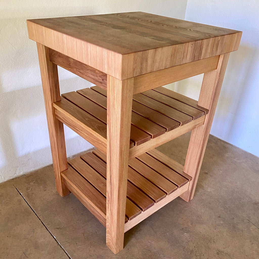 A end grain butcher island, made from pacific rimu with a middle slatted shelf, and a bottom slatted shelf, photographed in a room corner.