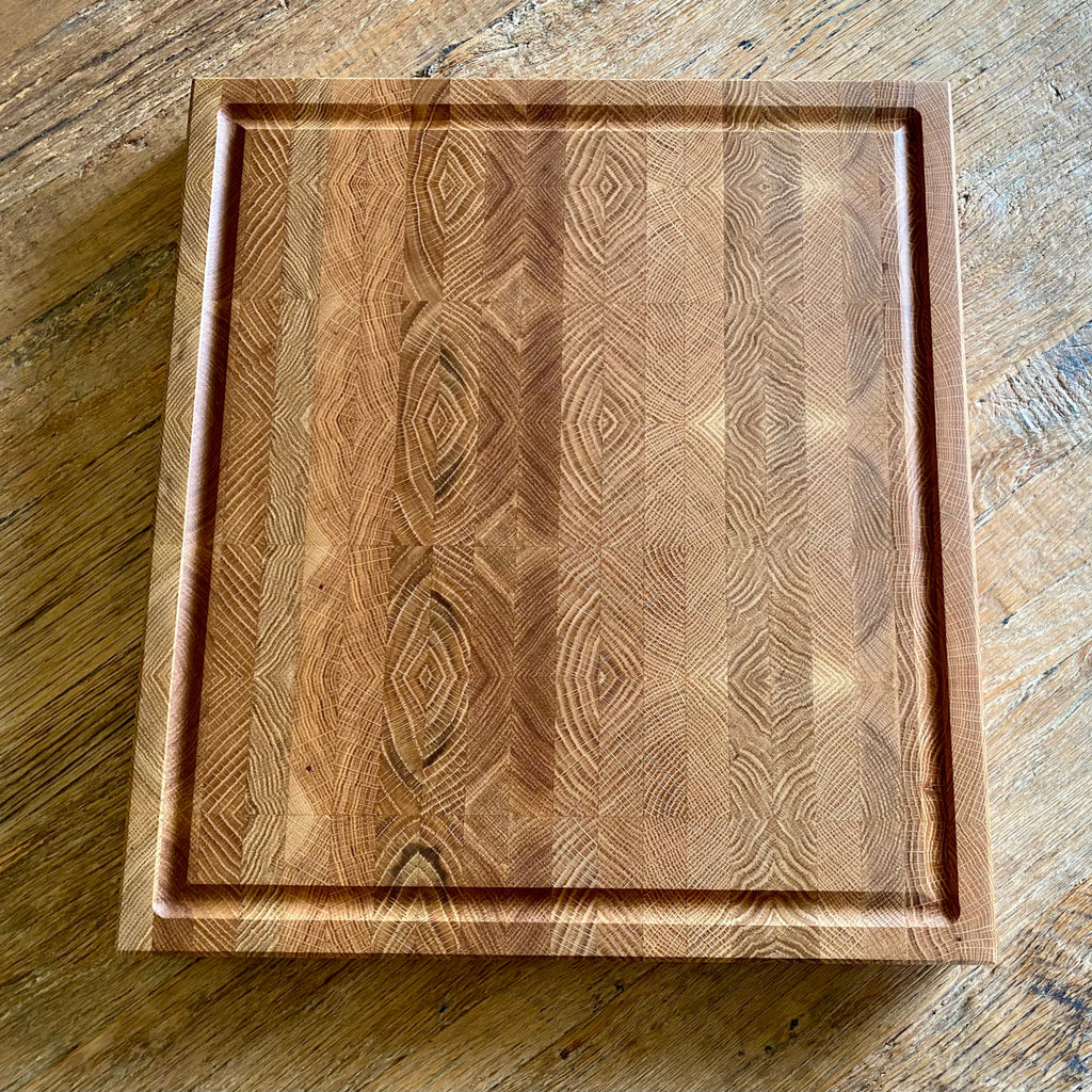 A rectangular whit oak end grain cutting board with a juice groove and a decorative geometric wood grain pattern, shown from a top-down perspective on a rustic wooden table.