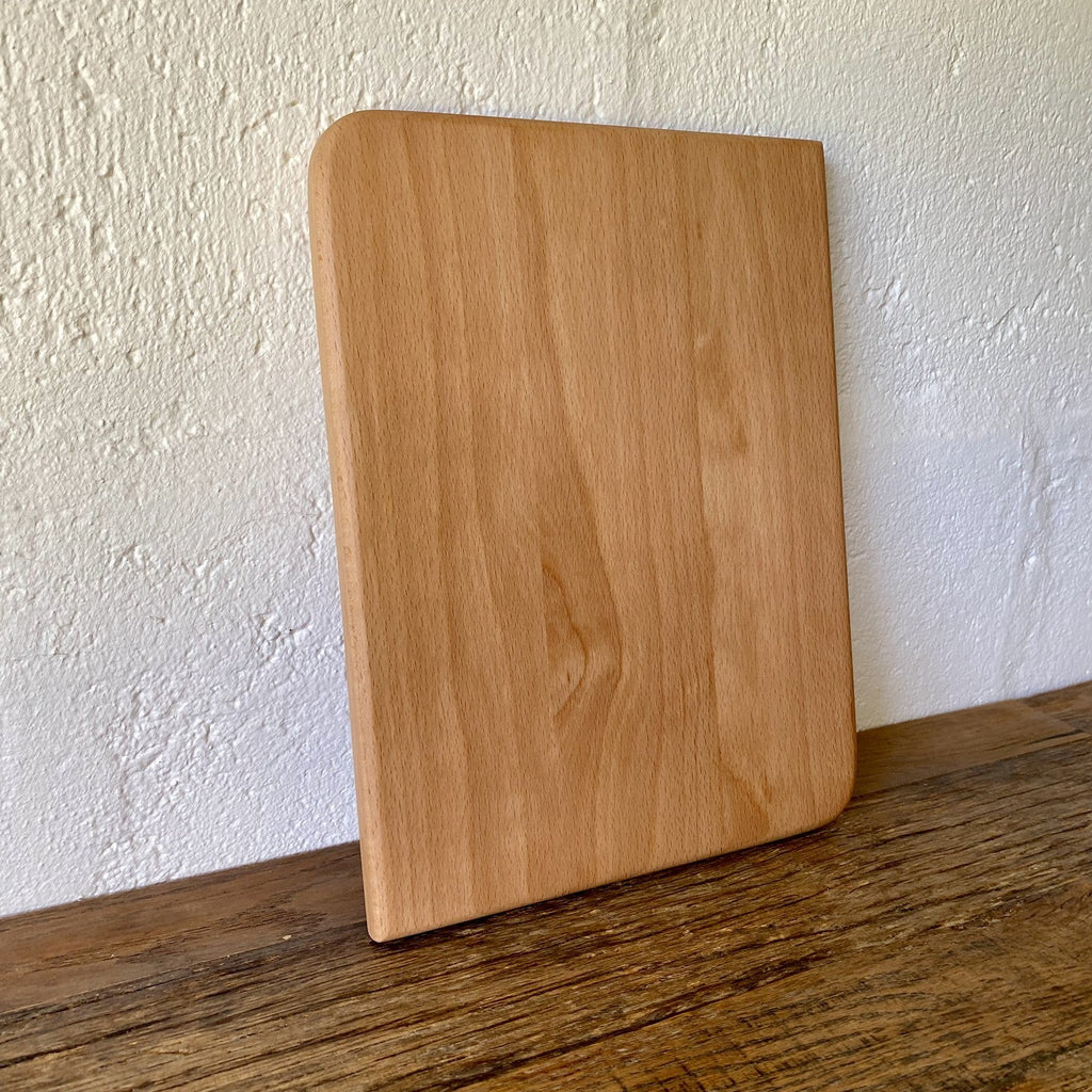 Small European beech chopping board leaning against white textured wall on timber surface – East Wood Design