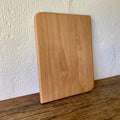 Small European beech chopping board leaning against white textured wall on timber surface – East Wood Design