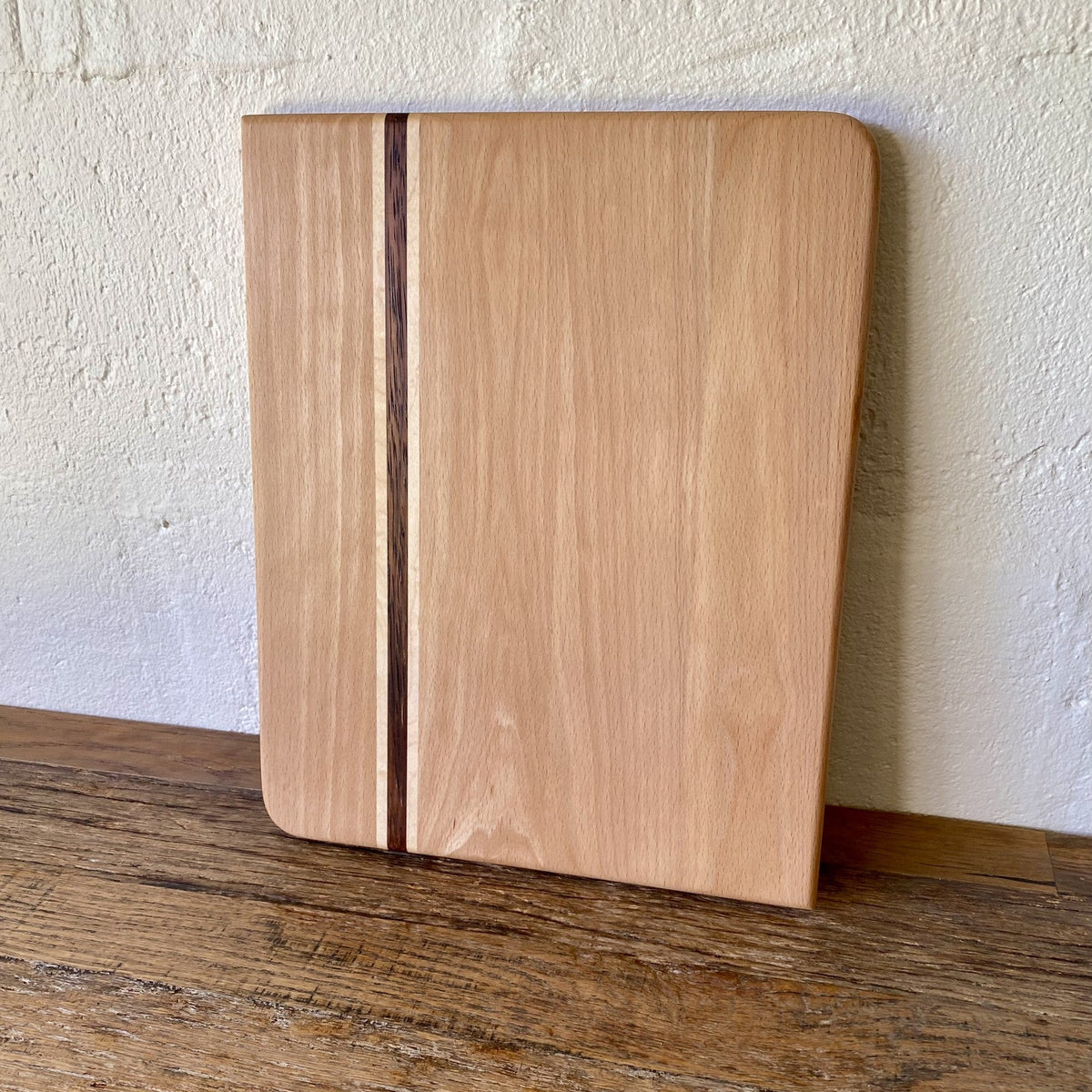 European beech chopping board with Kwila and maple stripe leaning against white wall on timber surface – East Wood Design