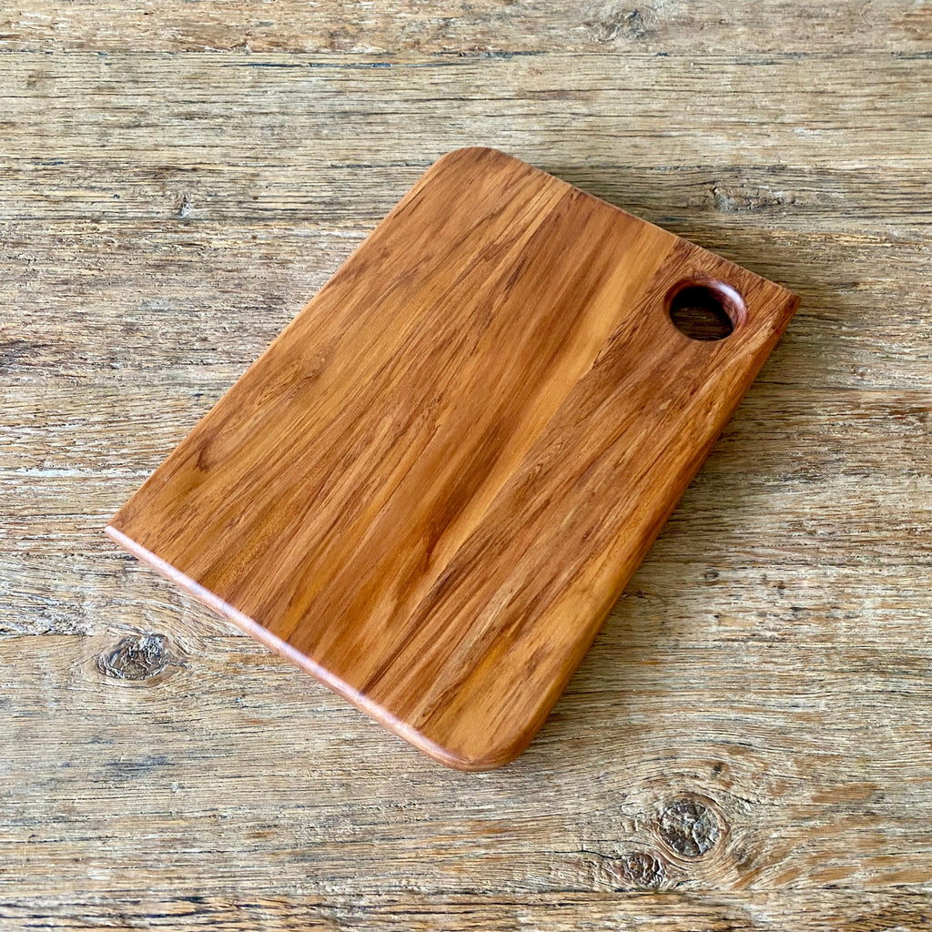 A rectangular heart Rimu wooden cutting board with rounded corners and a circular handle cutout, shown on a rustic wooden tabletop.