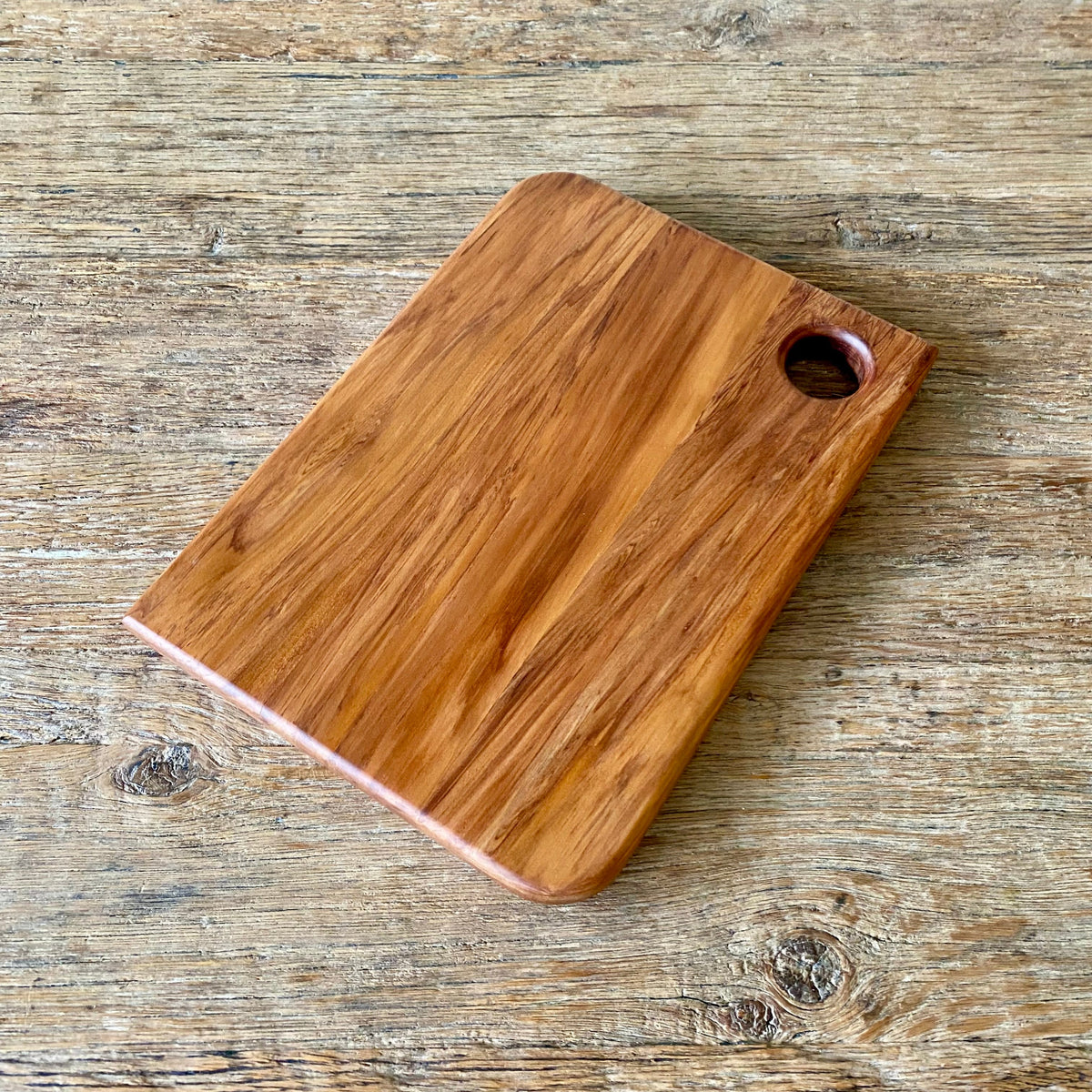 A rectangular heart Rimu wooden cutting board with rounded corners and a circular handle cutout, shown on a rustic wooden tabletop.