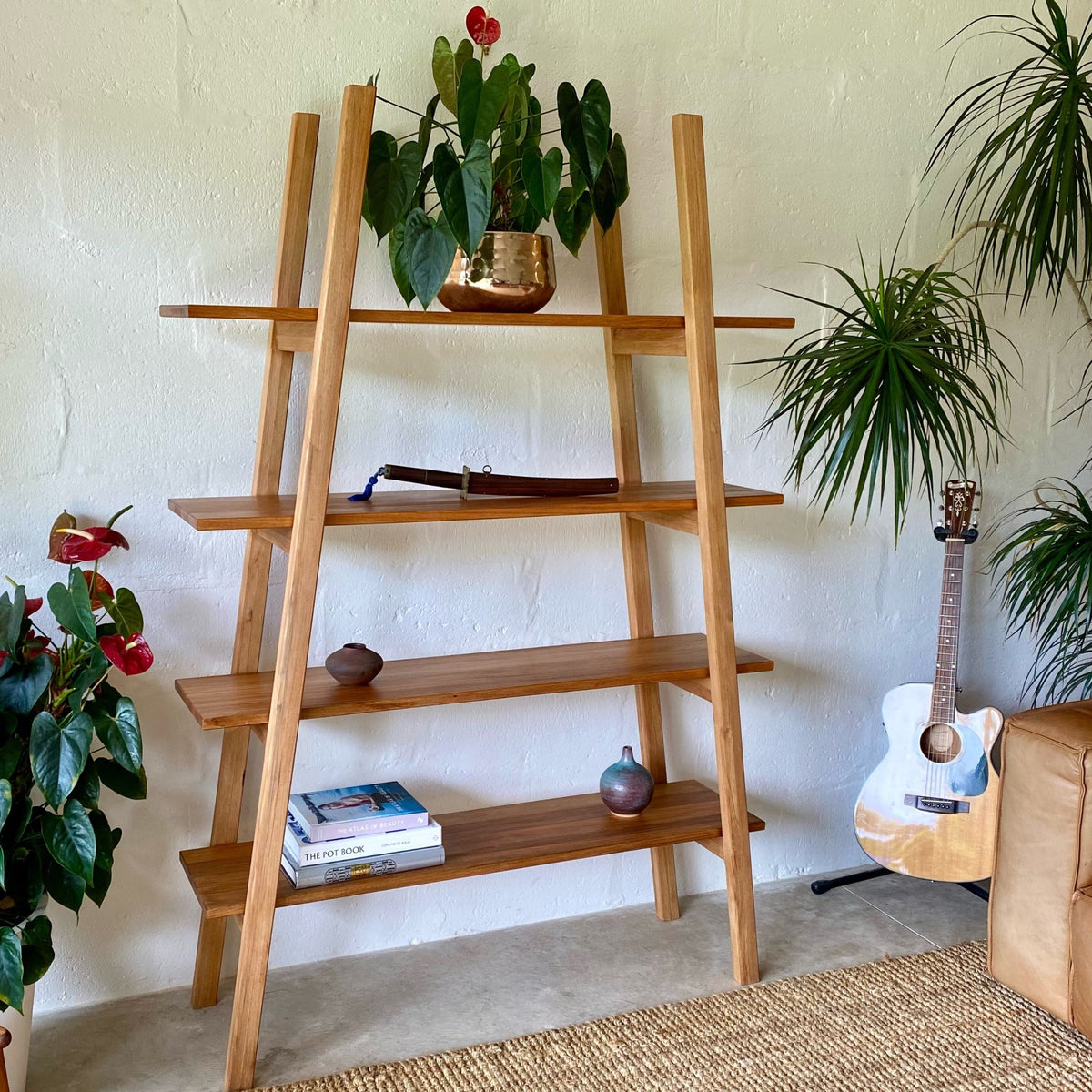 Ladder shelf stand in Pacific Rimu timber, front view in living room setting with plants and guitar