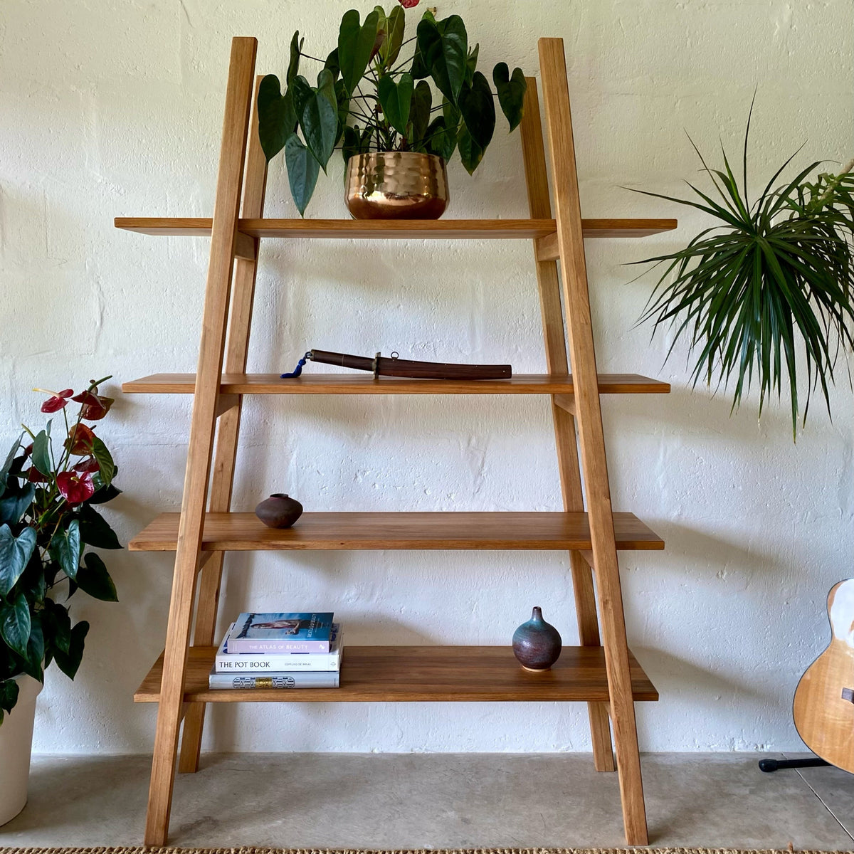 Ladder shelf stand in Pacific Rimu timber, three-quarter view showing full room context with lamp and plants