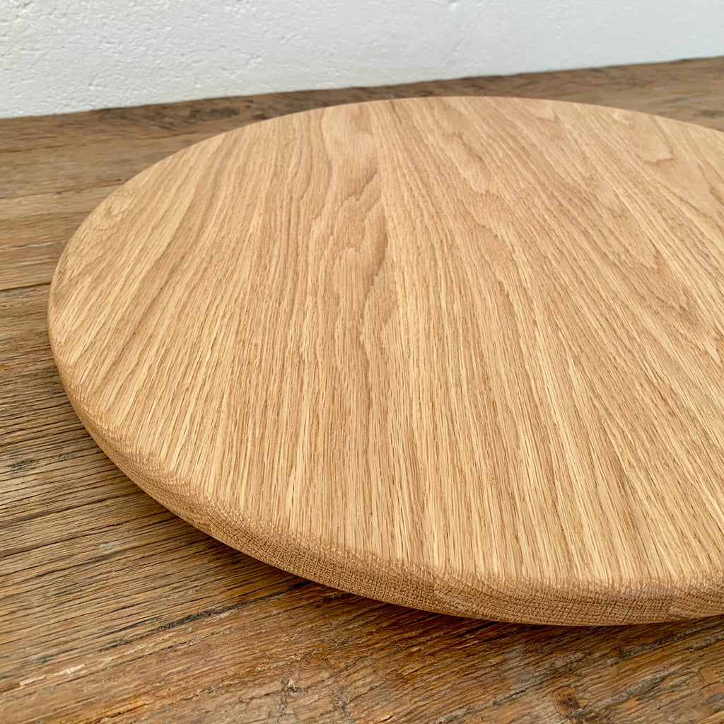 A round white oak lazy Susan, turntable with a natural oak finish, shown on a rustic wooden table against a white wall.