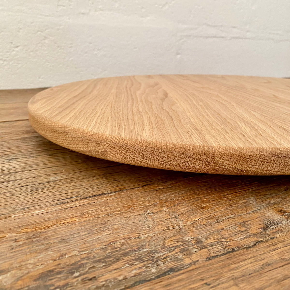 A round white oak lazy Susan, turntable with a natural oak grain, resting on a rustic wooden table against a white brick wall.