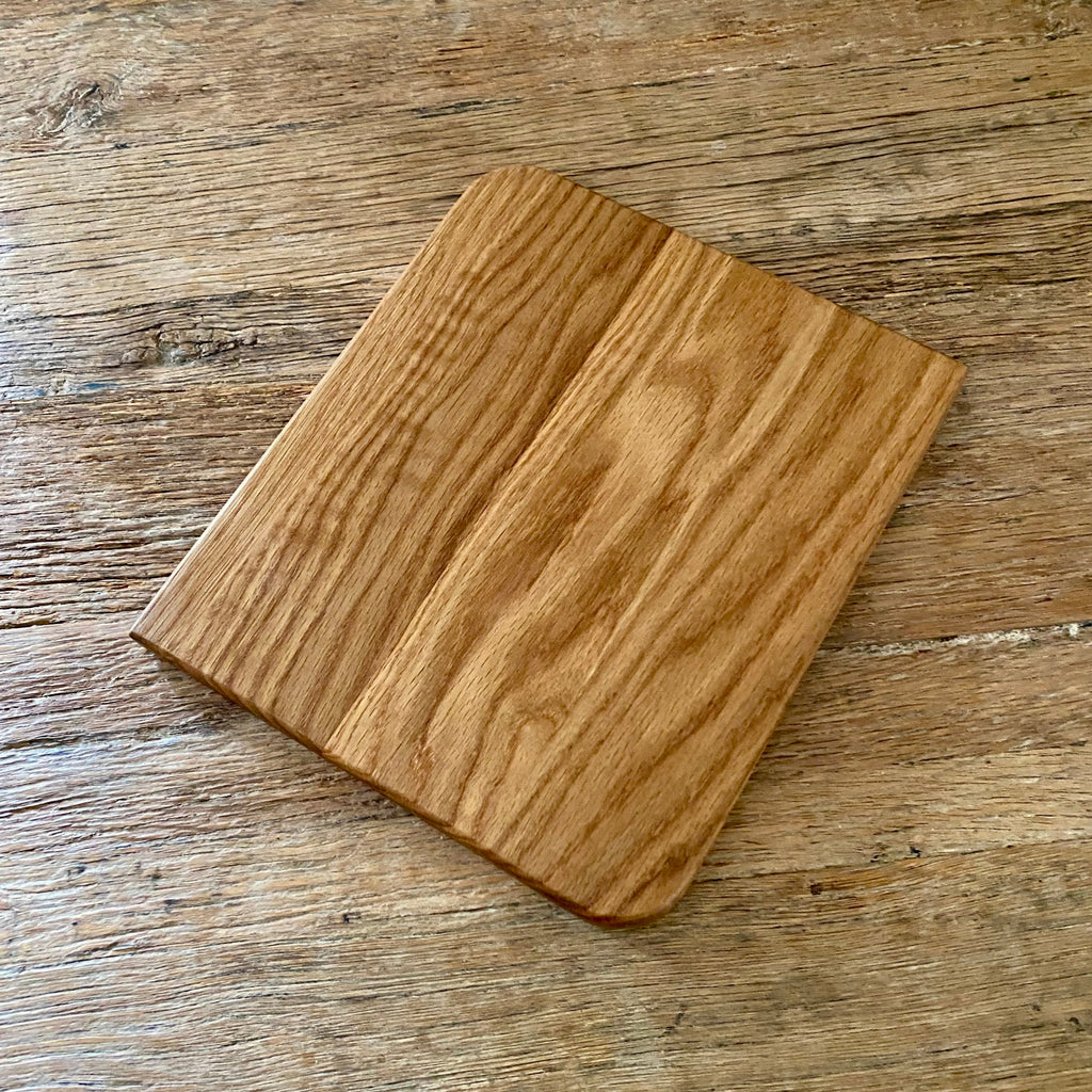 A square white oak wood cutting board with rounded corners and a smooth, polished surface, shown from an overhead angle on a rustic wooden table.