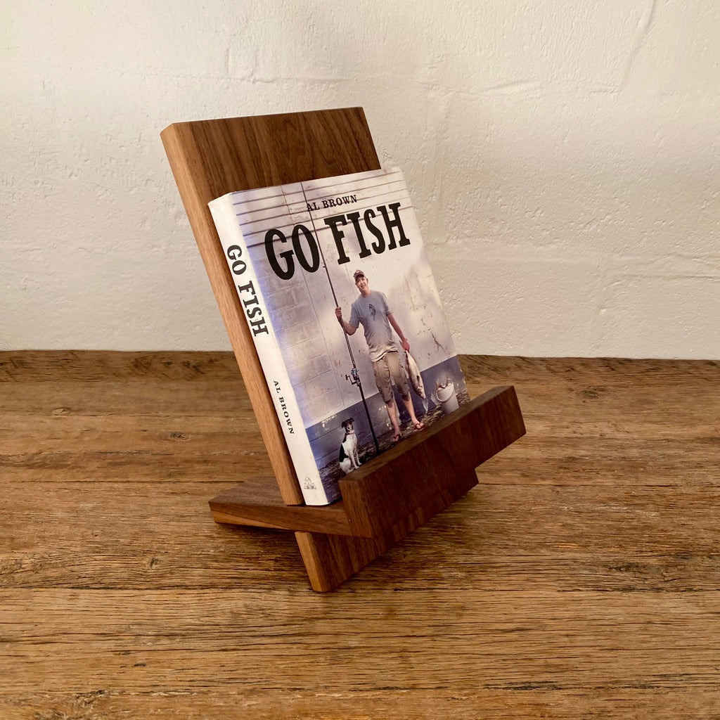 Book stand in Black Walnut holding a cookbook, angled view on rustic timber surface