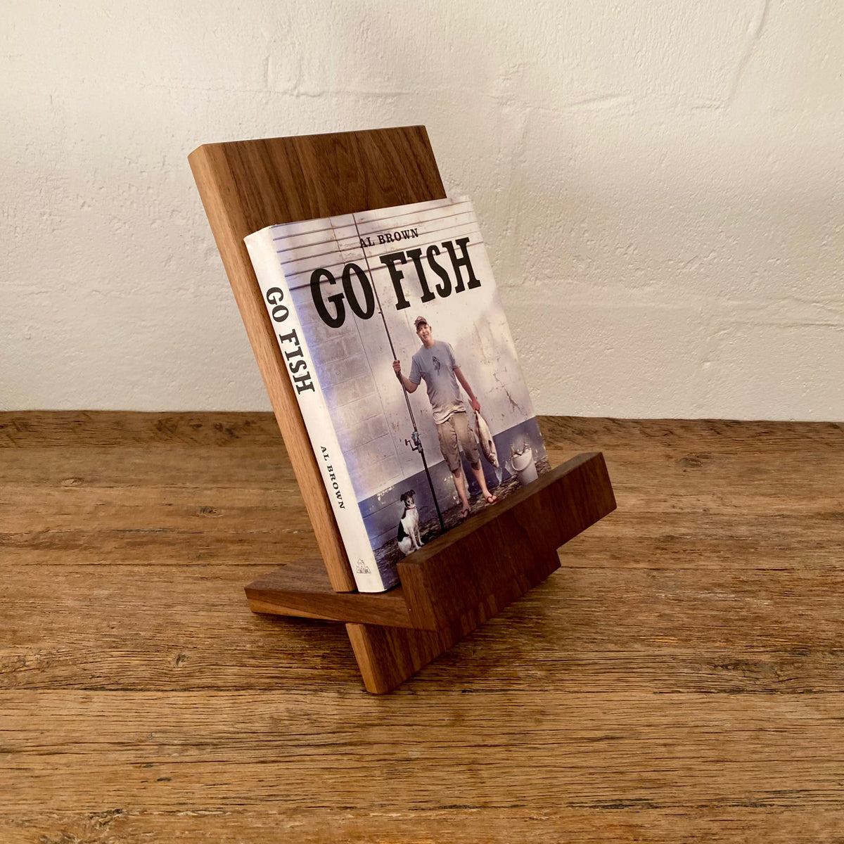Book stand in Black Walnut holding a cookbook, angled view on rustic timber surface