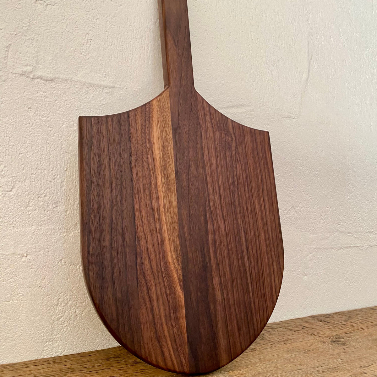 The Ray Board in American Black Walnut – front view leaning against white wall showing sting ray shape and handle