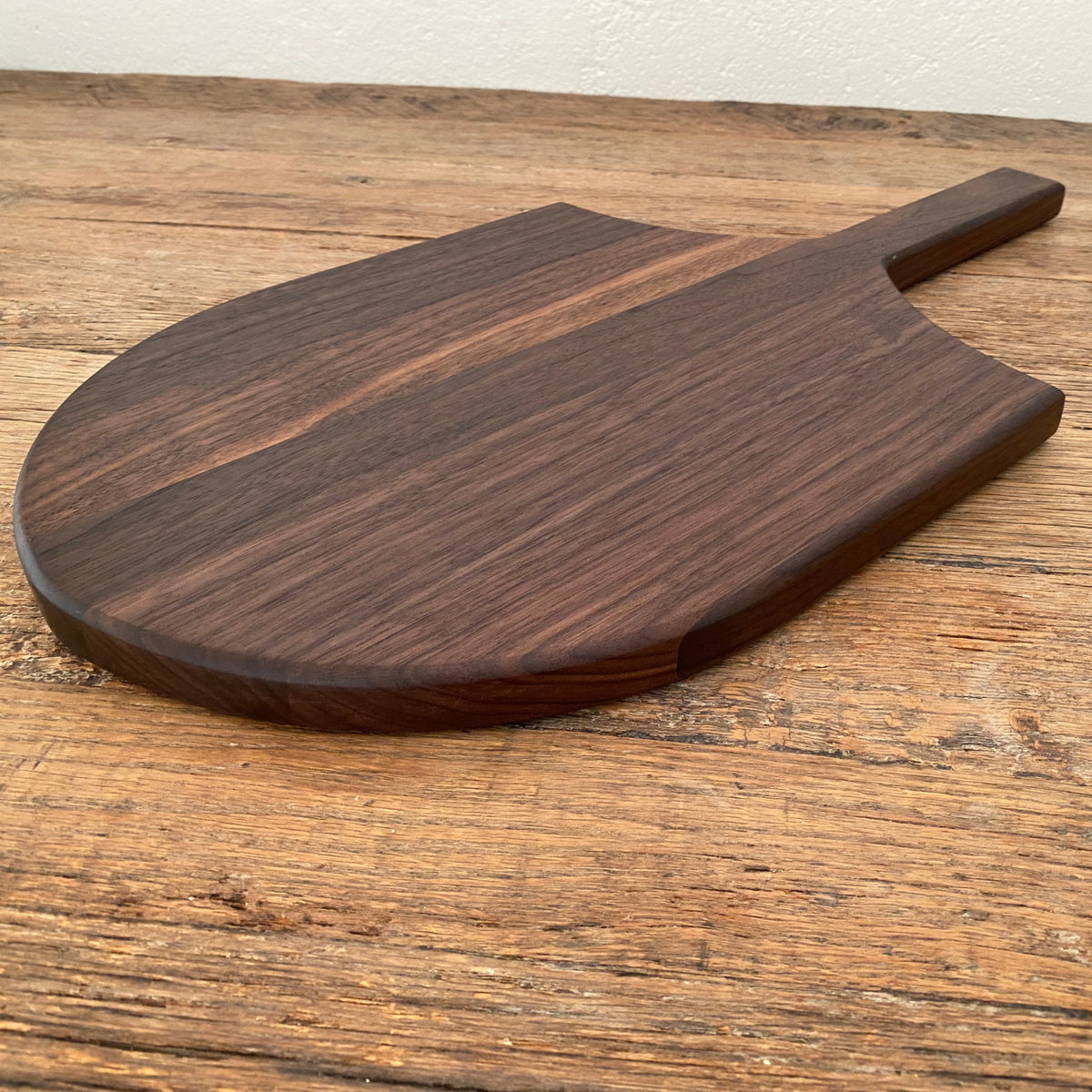 The Ray Board in American Black Walnut – side angle view on rustic timber surface showing board profile