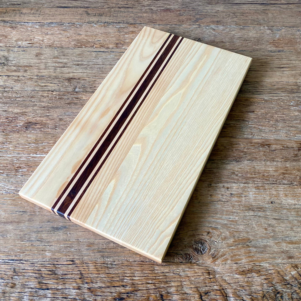 Ash Long platter Board with Kwila and Maple stripes running the length just off centre. The board is laying on a rustic table
