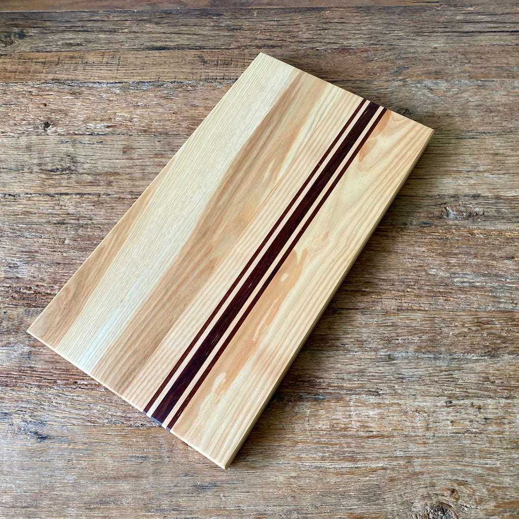Ash Long platter Board with Kwila and Maple stripes running the length just off centre. an angle view on a rustic table