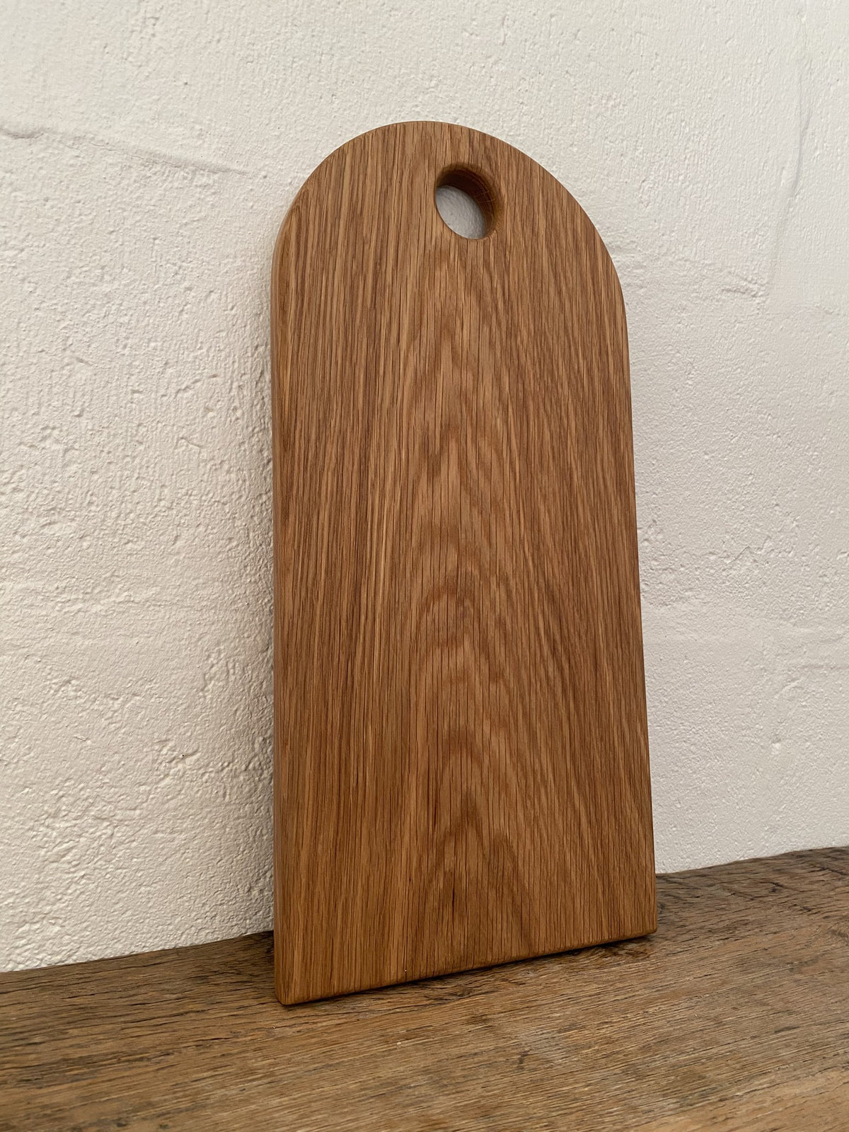 White oak arc platter arch shape leaning against white wall showing full profile and finger hole – East Wood Design