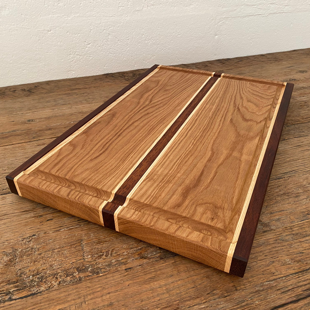 The Carver Grande chopping board in White Oak, Kwila and Maple – angled side view showing timber stripe detail and juice groove on rustic surface