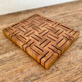A rectangular white oak and kwila wooden cutting board with a juice groove and geometric inlay pattern of dark brown and medium brown wood blocks, on a rustic wooden table